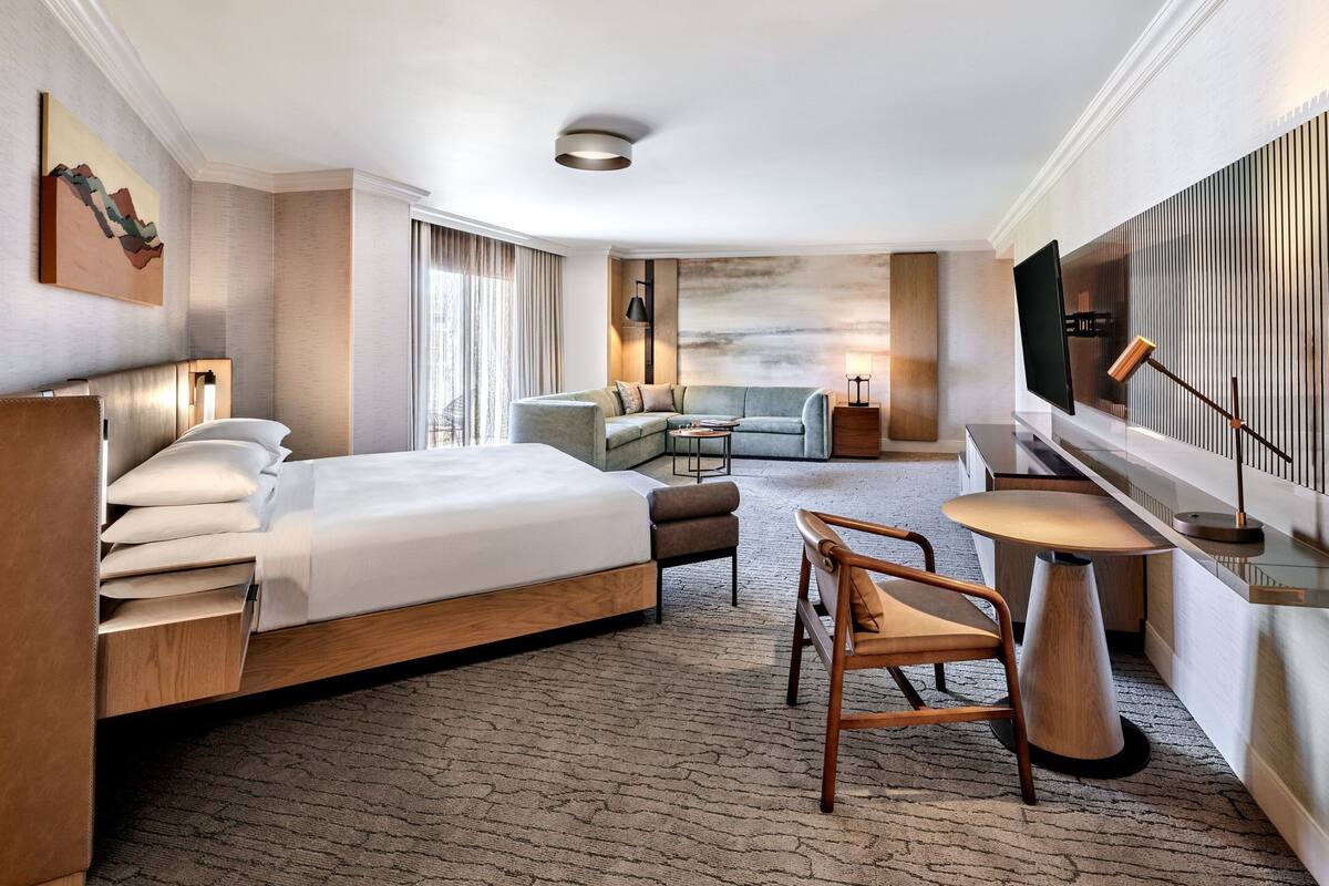 A modern hotel room with a large bed, a sofa, a small table, and a TV.