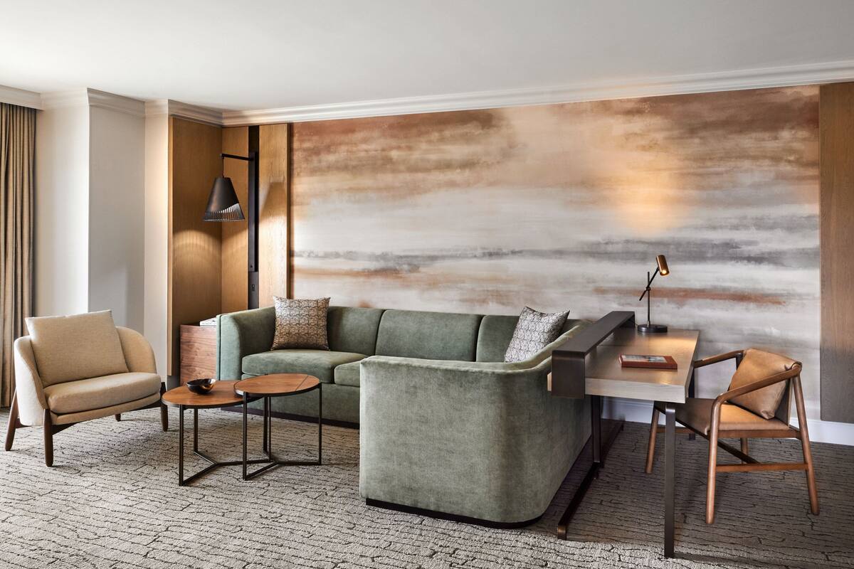 A modern living room with a sectional sofa, a small round table, a desk with a lamp, and a large abstract wall mural.