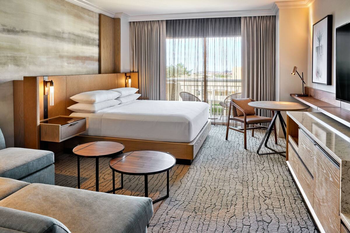 A hotel room with a large bed, bedside tables, a desk with a chair, a small round table, and a TV.