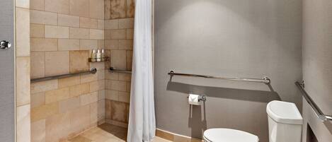 A modern bathroom with a shower, toilet, and handrails.