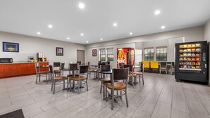 A spacious dining area with multiple tables and chairs, vending machines, and a counter with a beverage dispenser. - Days Inn by Wyndham near Kansas Speedway (Kansas City)