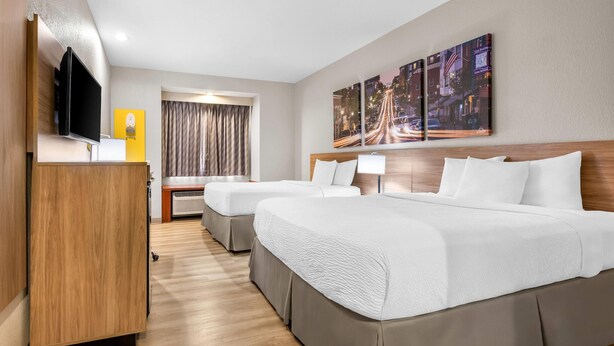 A hotel room with two beds, a TV, a desk, a window with curtains, and a cityscape painting on the wall. - Days Inn by Wyndham near Kansas Speedway (Kansas City)