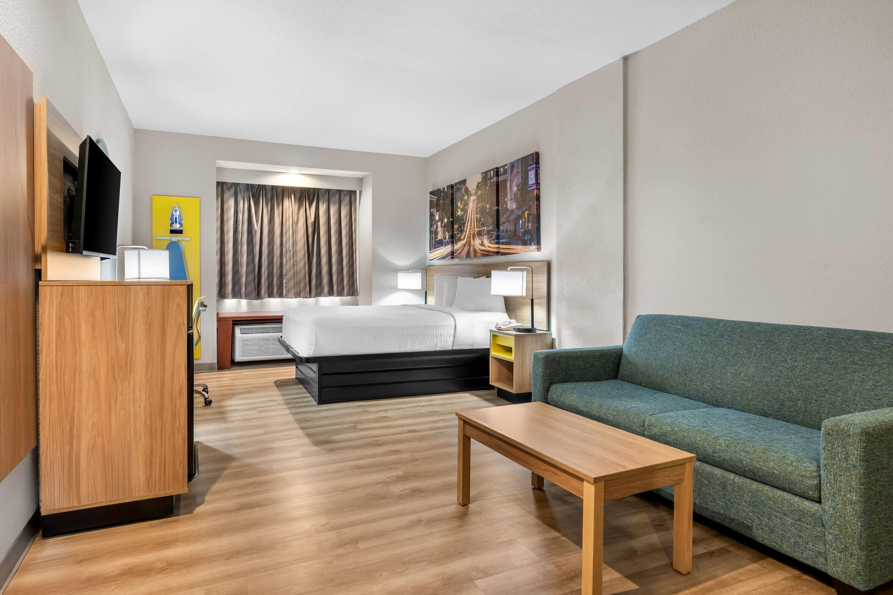 A hotel room with a bed, a desk, a sofa, a television, and a painting on the wall.