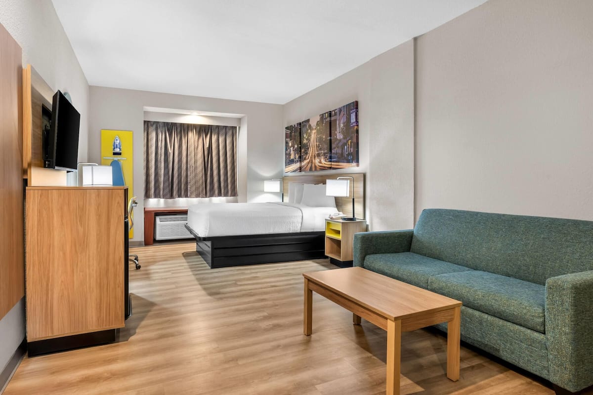 A hotel room with a bed, a desk, a sofa, a television, and a painting on the wall.