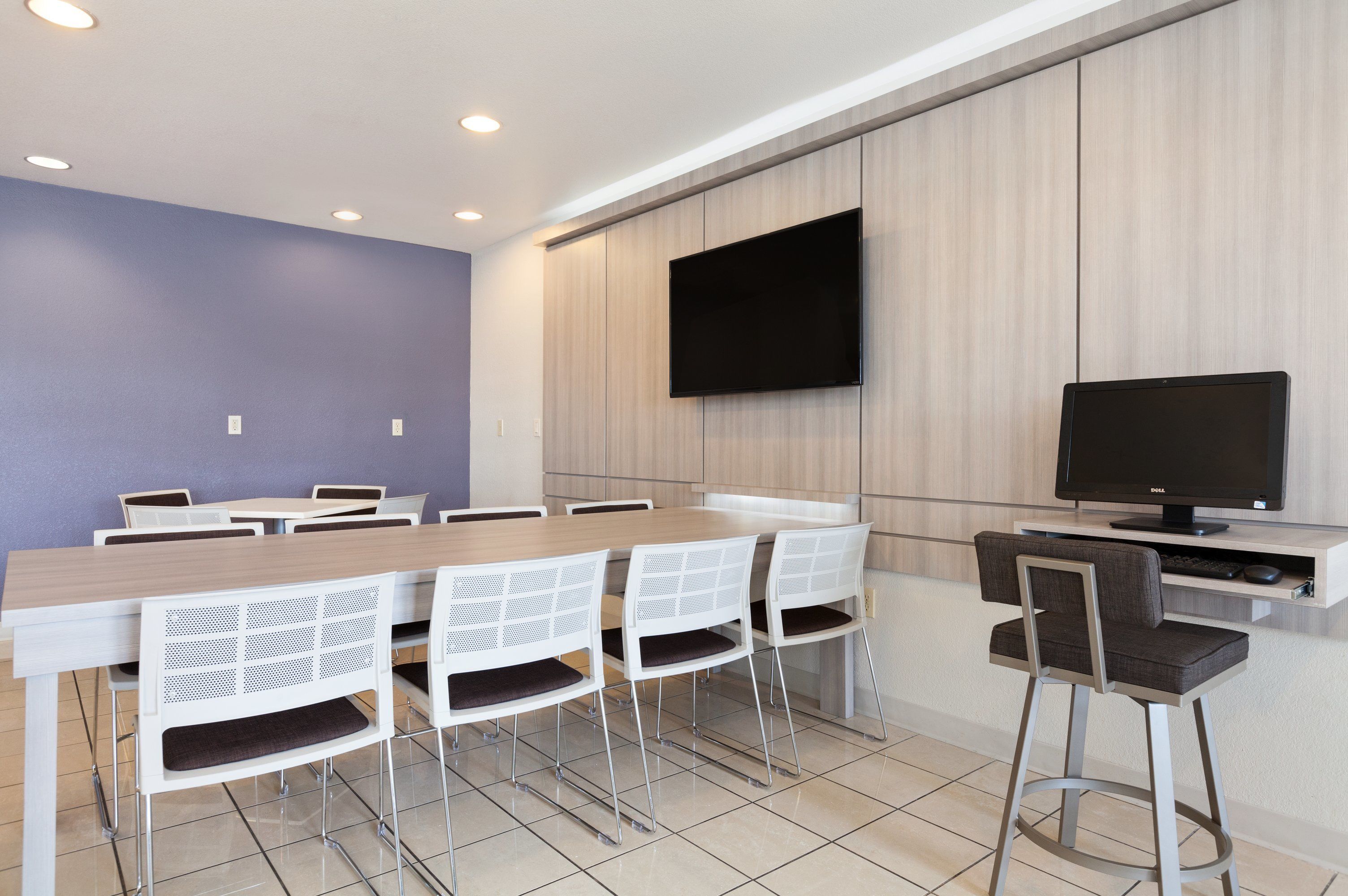 Una sala de conferencias moderna con una larga mesa, sillas blancas, un televisor de pantalla plana y una pared de acento de madera.
