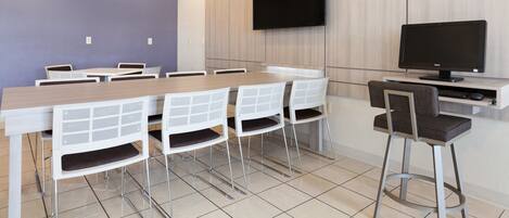 A modern conference room with a long table, white chairs, a flat-screen TV, and a wooden accent wall.