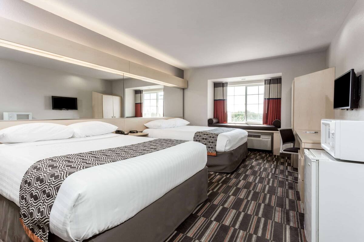 Una habitación de hotel con dos camas, un escritorio, un televisor y un microondas.