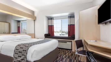 A hotel room with a bed, a desk, a chair, a TV, and a window with curtains.