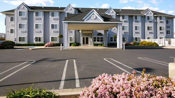 A multi-story hotel with a covered entrance, parking lot, and landscaping.