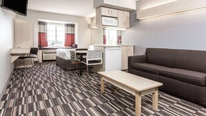 A compact room with a kitchenette, a sofa, a dining area with a table and chairs, and a TV mounted on the wall.