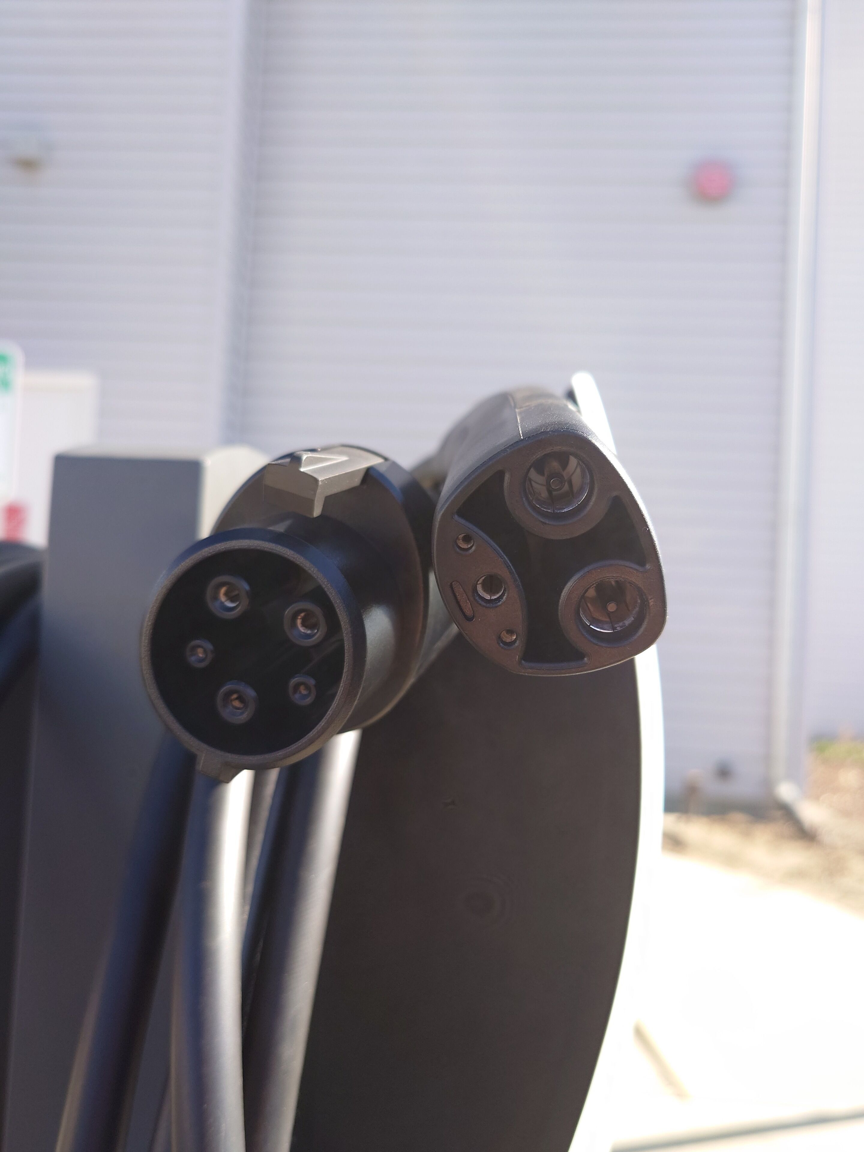 A close-up of a black cable with a connector, likely for an electric vehicle charging station, attached to a gray metal structure.