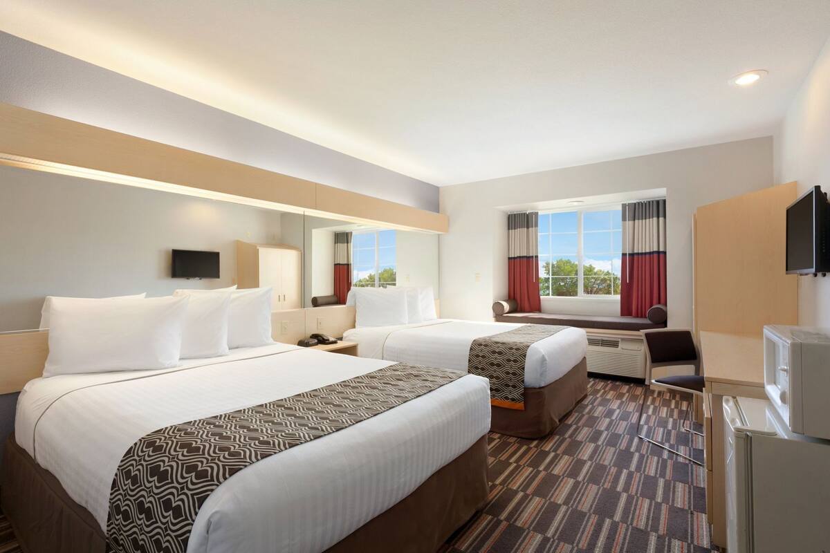 Habitación de hotel con dos camas, un escritorio, un televisor y una ventana con cortinas.