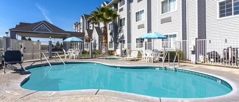 A swimming pool with a curved edge, surrounded by a white fence and lounge chairs.