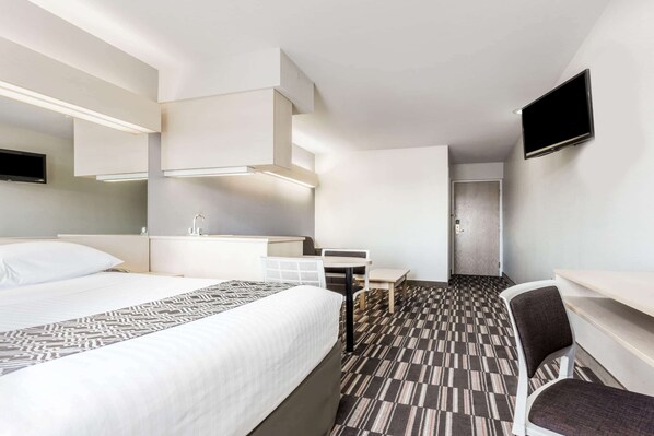 A hotel room with a bed, a desk, a chair, a TV, and a patterned carpet.