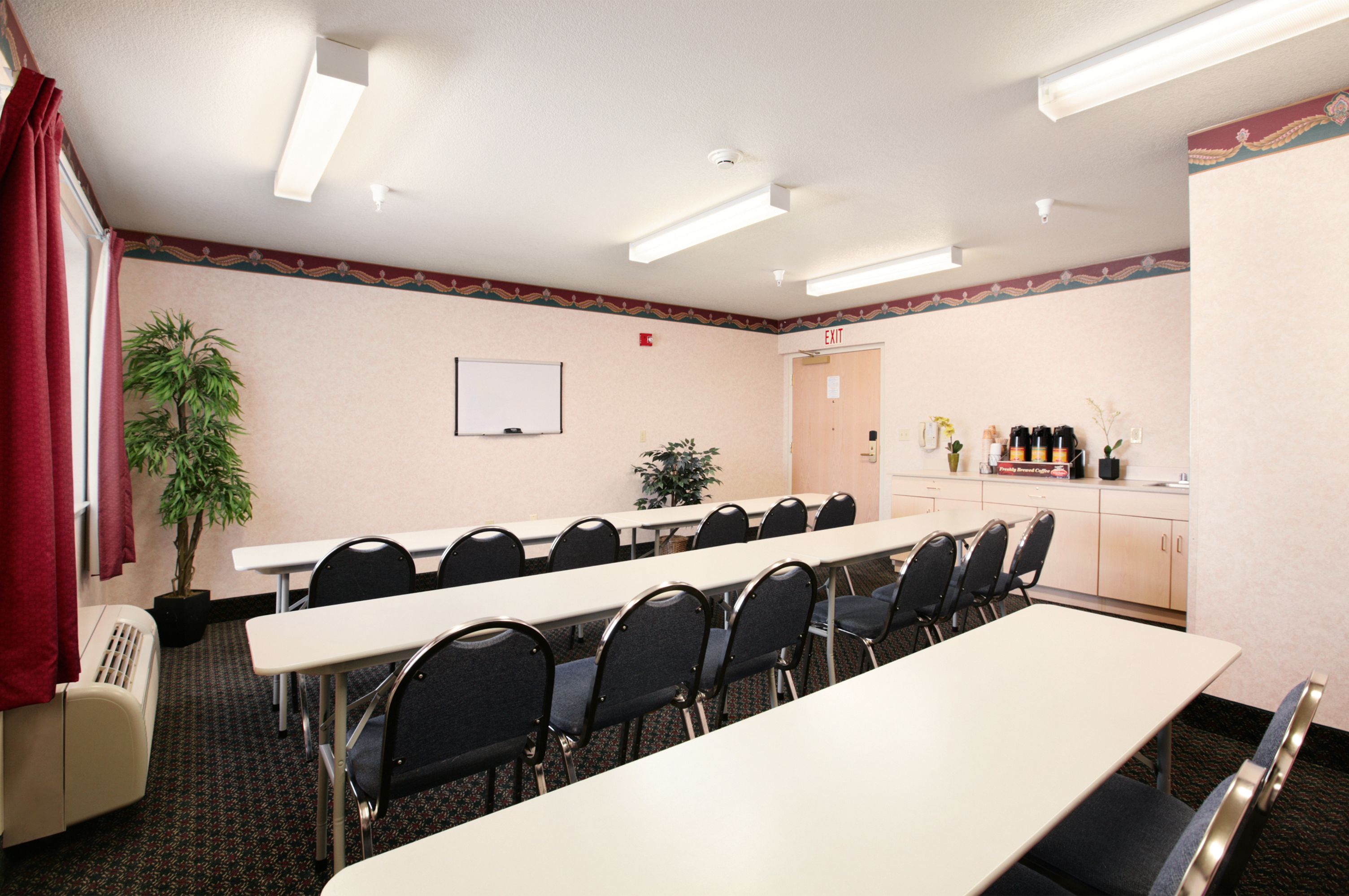 Une salle de conférence équipée d’une longue table, de chaises, d’un tableau blanc et d’un coin cuisine.