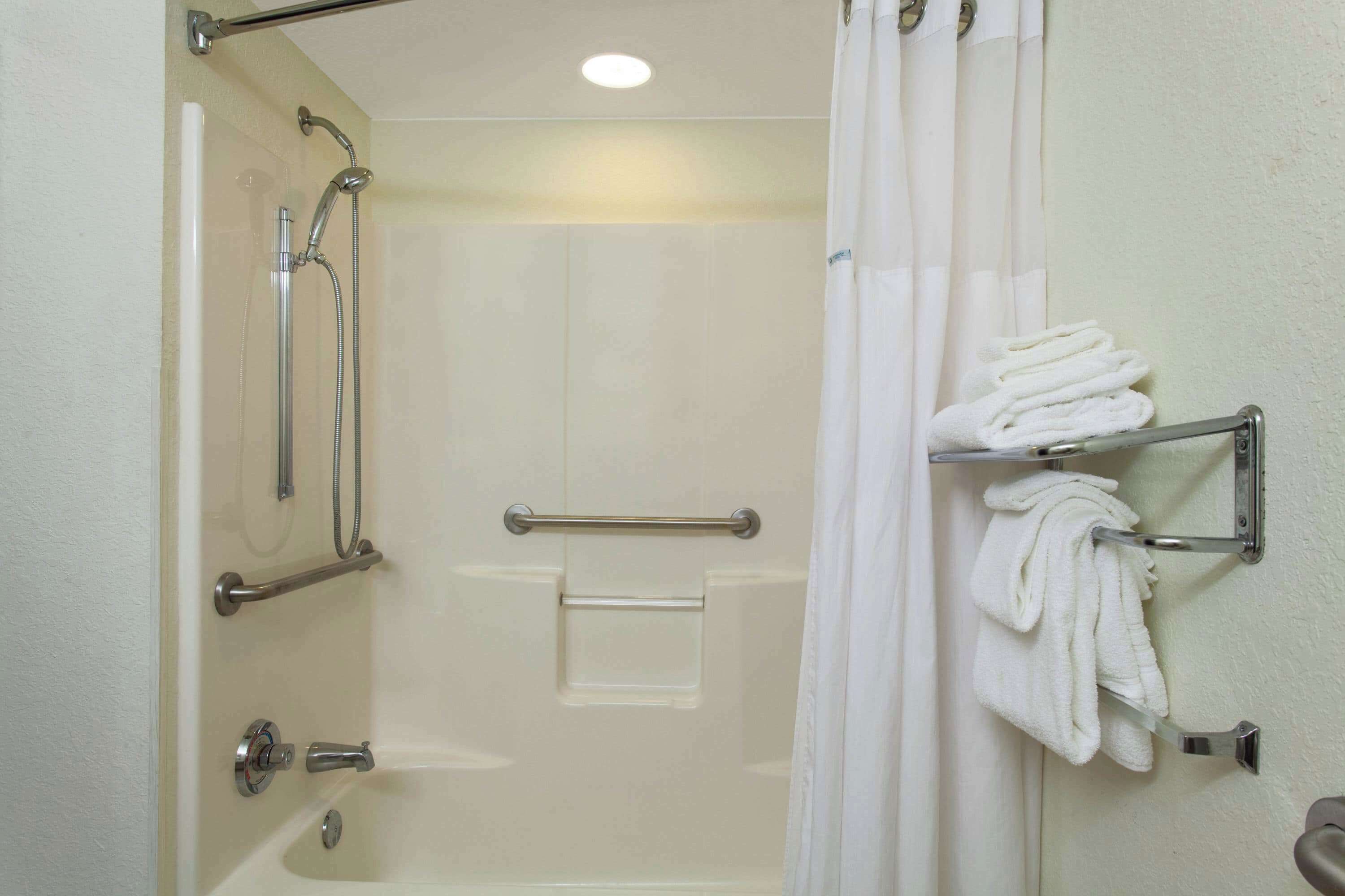A bathroom with a shower, grab bars, a towel rack, and a toilet.