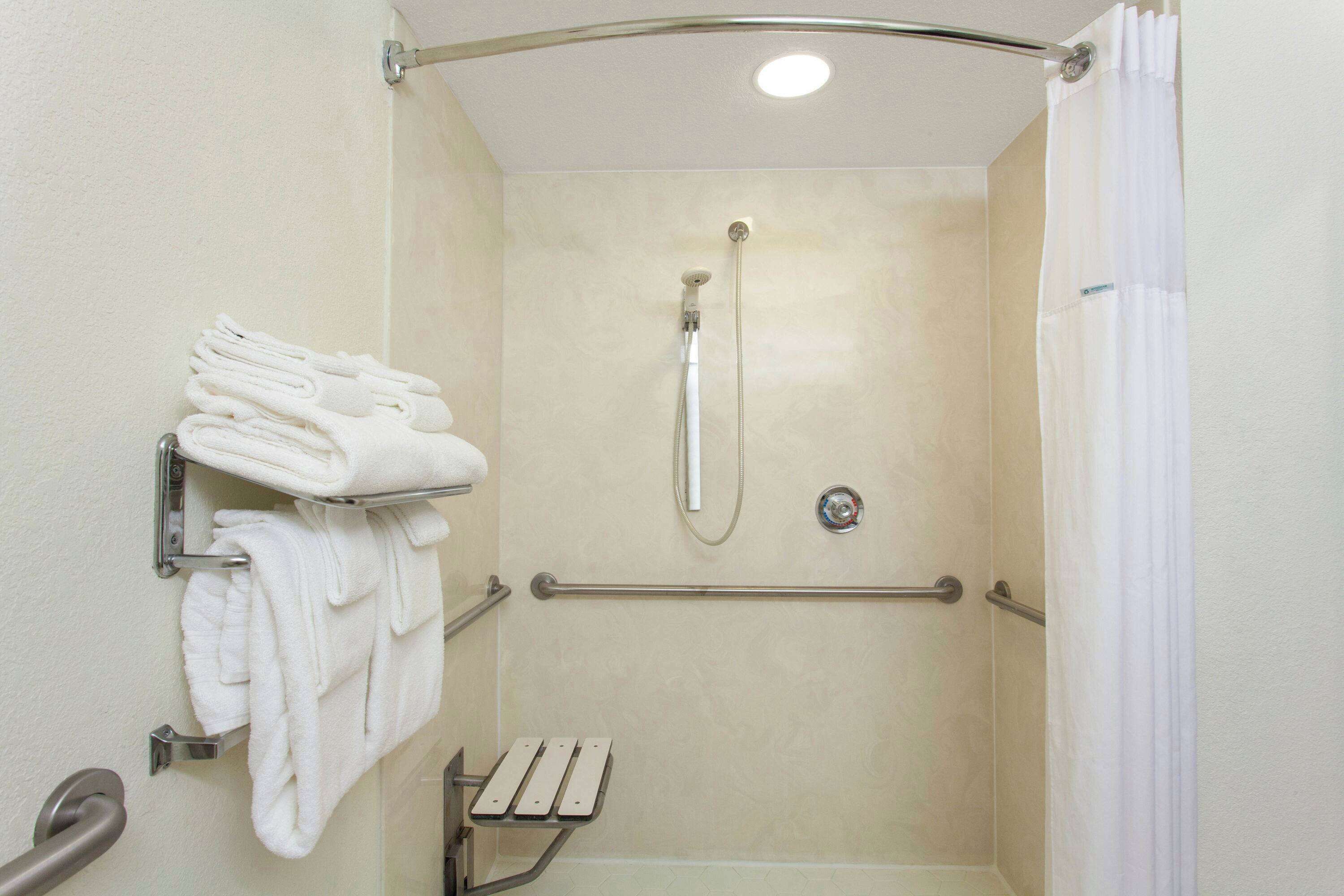 Een douche met een handdouche, handgrepen en een handdoekrek met opgevouwen handdoeken.