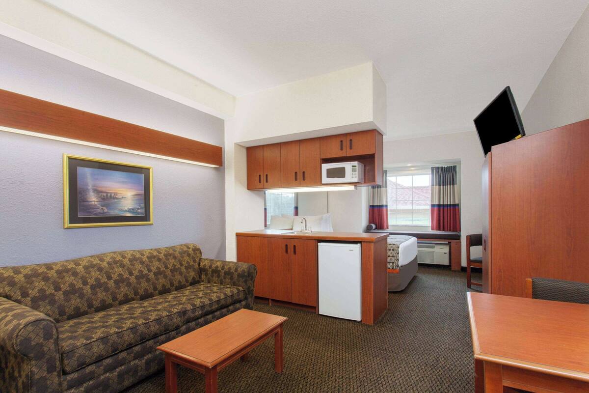 Une chambre d’hôtel compacte comprenant un coin cuisine, un canapé, une petite table et un téléviseur.