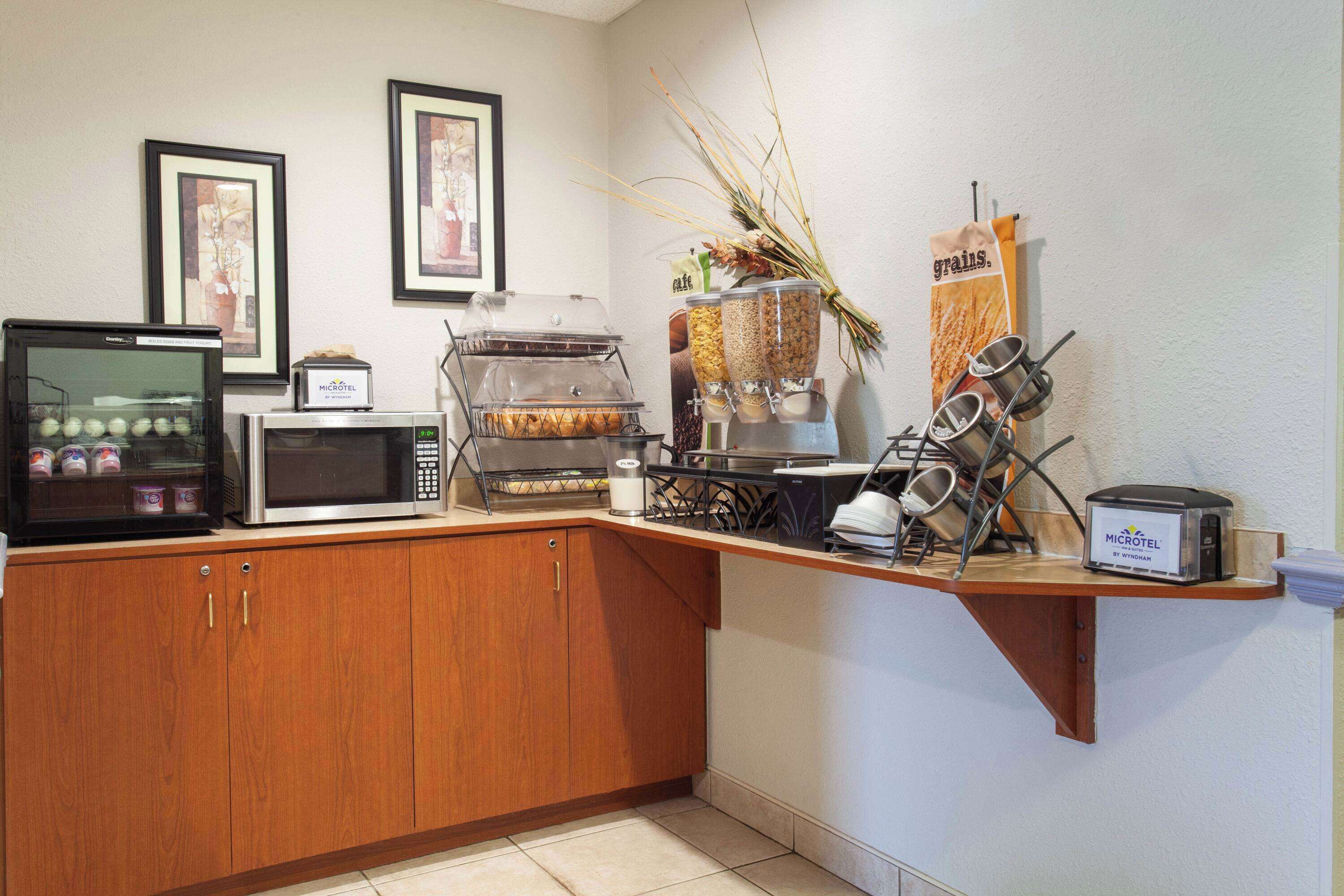 A kitchenette with a microwave, toaster, and coffee maker. There are also containers of grains and a hanging rack with utensils.