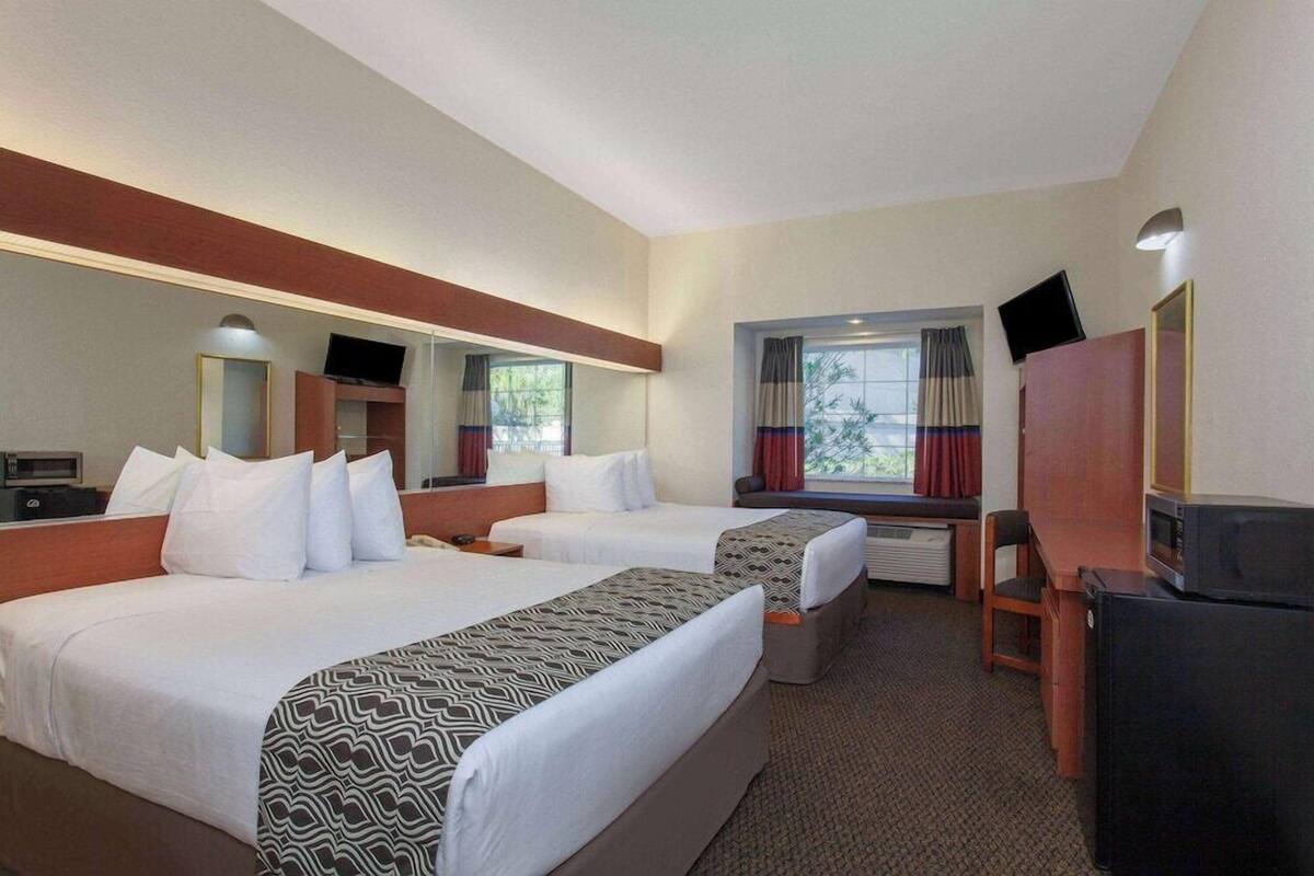A hotel room with two beds, a desk, a television, and a window with curtains.