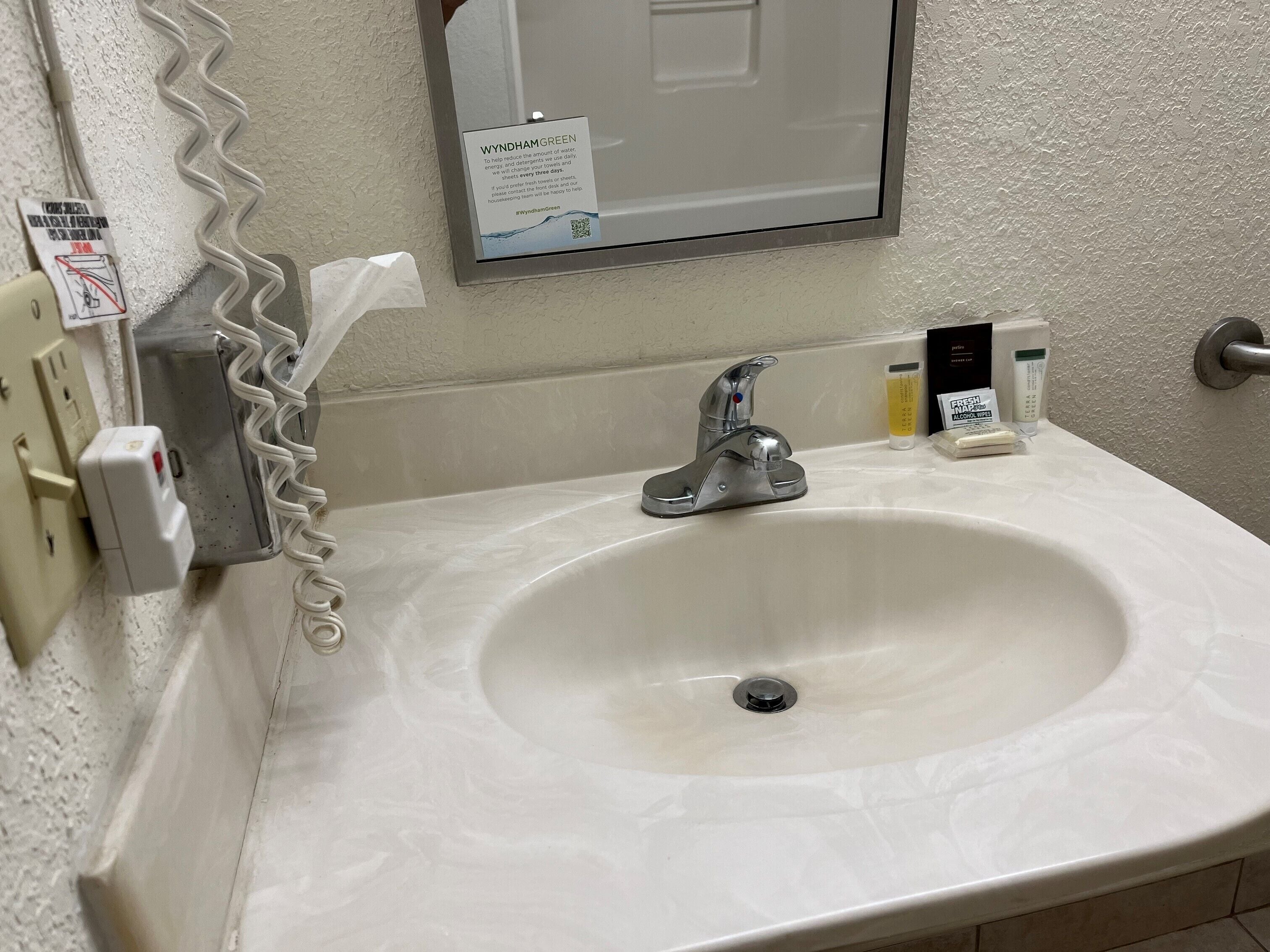 A bathroom sink with a mirror above it, a hand dryer, and a hand soap dispenser.