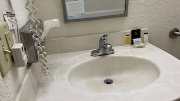 A bathroom sink with a mirror above it, a hand dryer, and a hand soap dispenser.