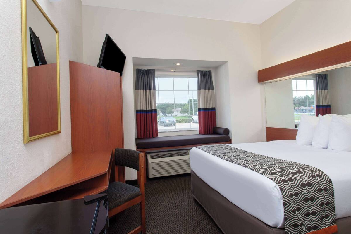 Une chambre d’hôtel avec un grand lit, un bureau, une chaise, une fenêtre avec des rideaux et une vue sur l’extérieur.
