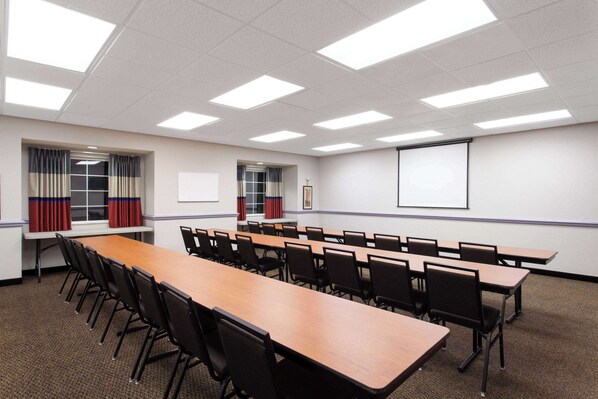 A conference room with a long table, chairs, a projector screen, and windows with curtains.