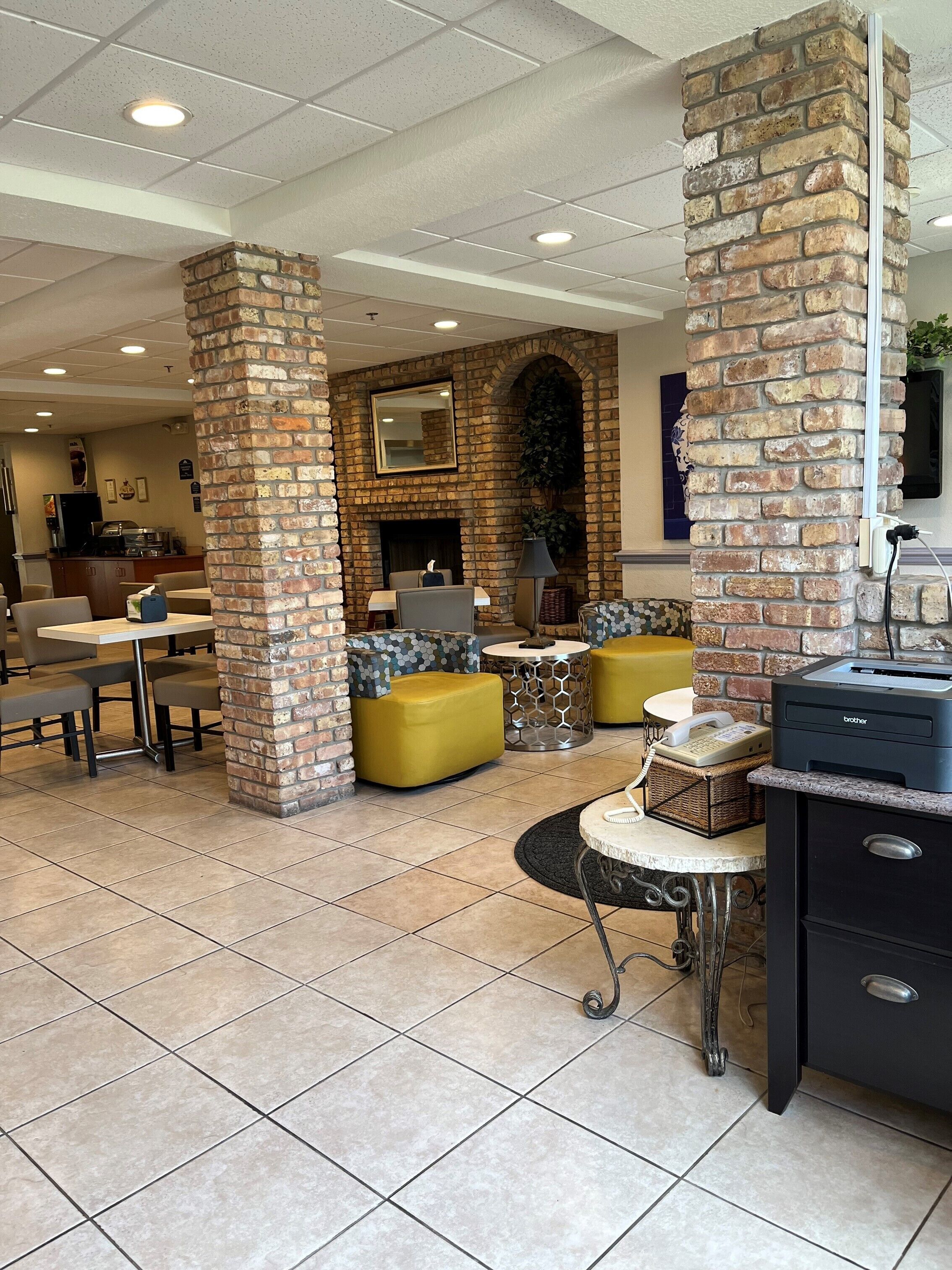 A lobby with brick pillars, a fireplace, seating areas, and a Brother printer on a counter.