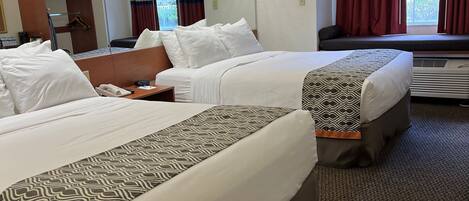 A hotel room with two beds, a desk, a chair, a TV, and a window with curtains.
