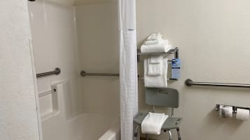 A bathroom with a shower, grab bars, a wheelchair-accessible bench, and a towel rack.
