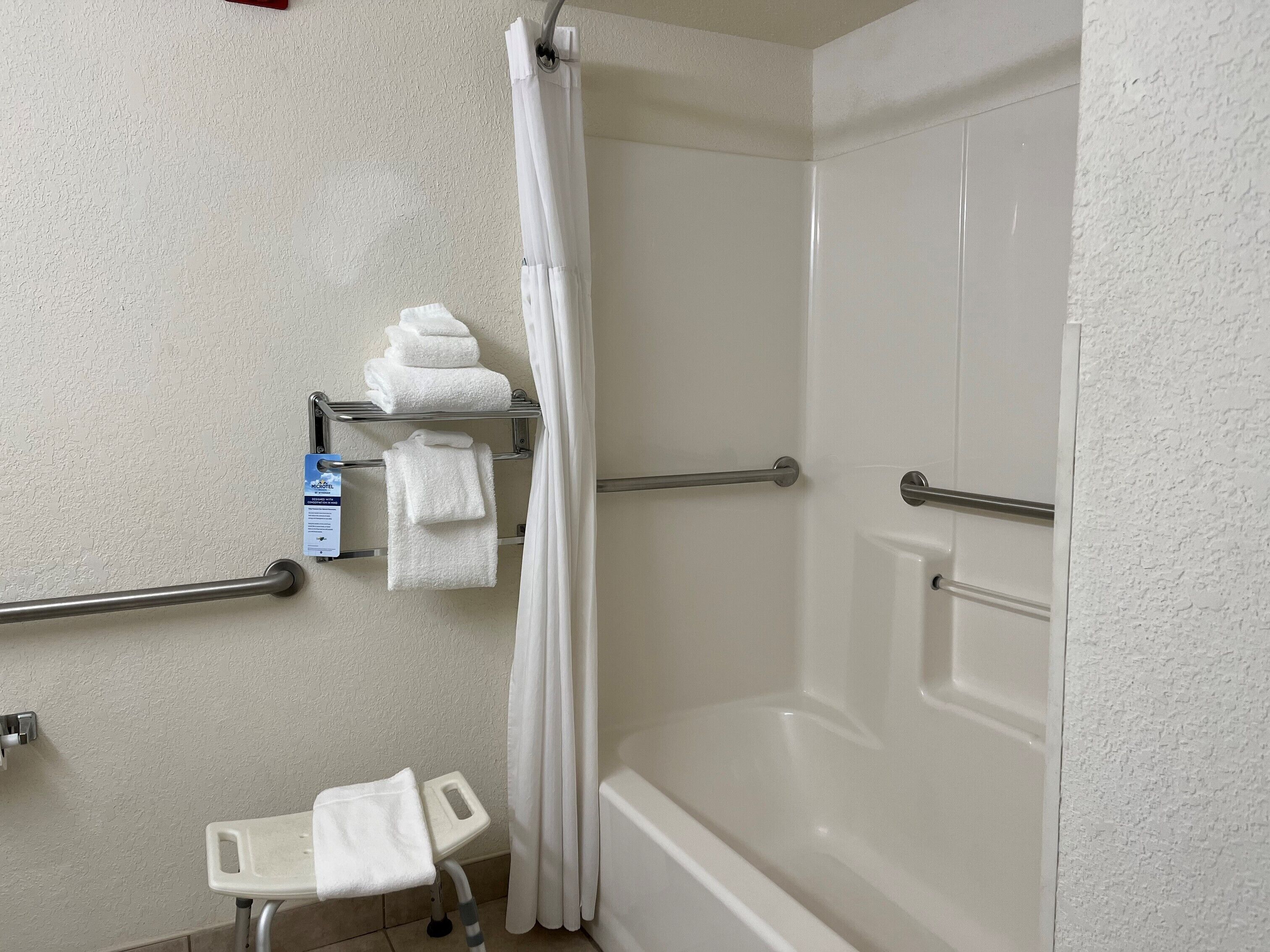 Un baño con ducha, inodoro y lavabo. Hay toallas en un perchero y una cortina de ducha.