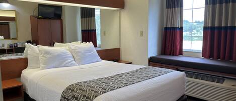 Habitación de hotel con una cama grande, una mesita de noche, un espejo, una ventana con cortinas y un equipo de aire acondicionado integrado.
