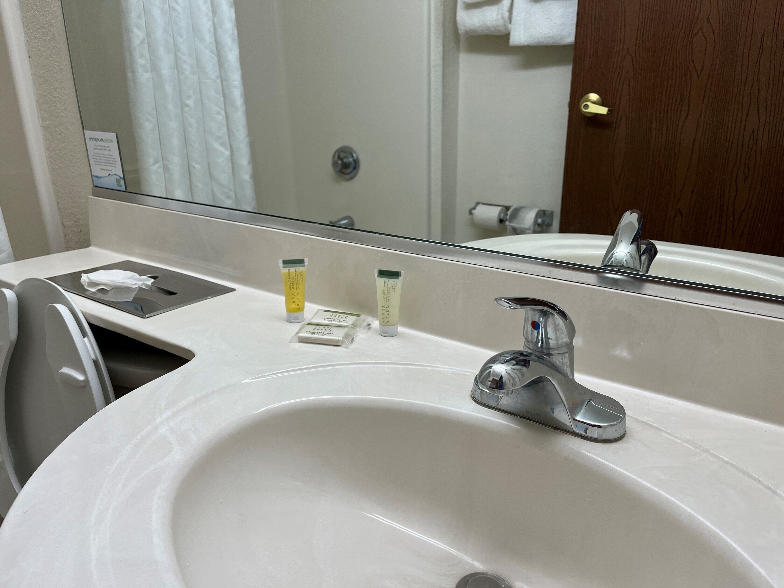 A hotel bathroom with a sink, mirror, and toiletries.