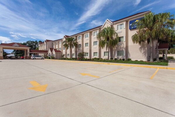 A hotel with a parking lot, marked parking spaces, and a building facade with a sign. - Microtel Inn & Suites by Wyndham Lady Lake/The Villages (Lady Lake)