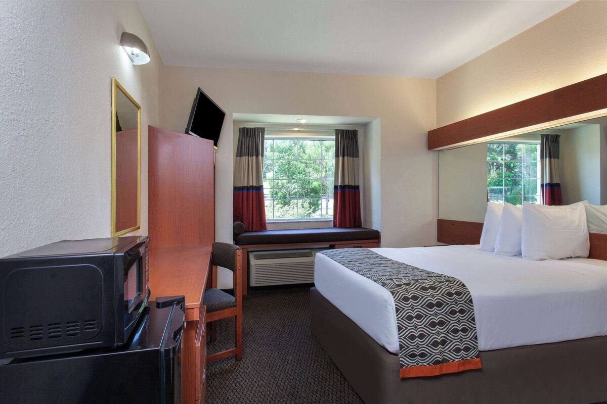 Une chambre d’hôtel avec un lit, un bureau avec une télévision, une fenêtre avec des rideaux et un miroir.