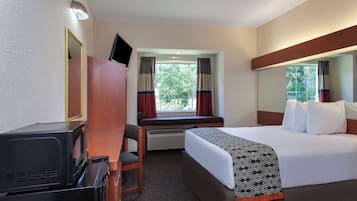 Quarto de hotel com cama, escrivaninha com televisão, janela com cortinas e espelho.