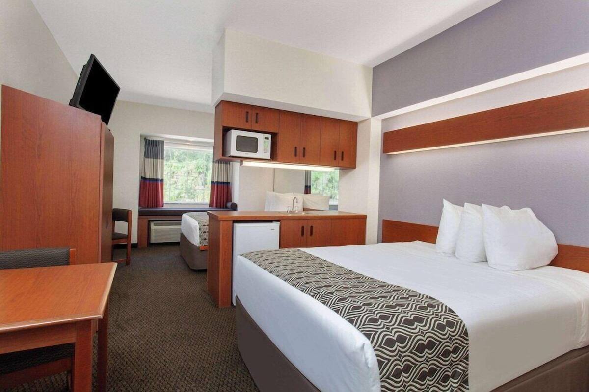A hotel room with a bed, a desk, a microwave, a small refrigerator, and a television.