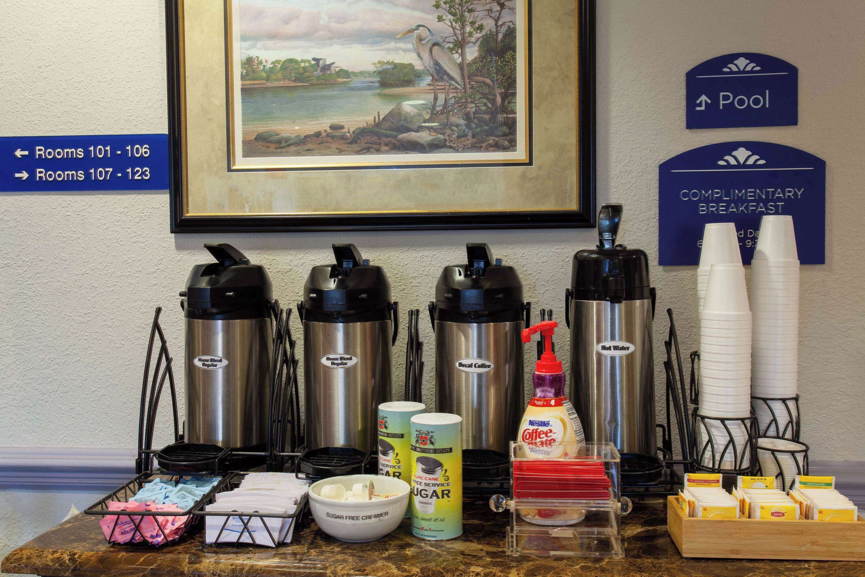 Un buffet pour le petit-déjeuner comprenant des machines à café, du substitut de crème sans sucre, de la crème pour café, des sachets de sucre et divers condiments.