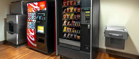 A vending machine with snacks and a Coca-Cola machine in a room with wooden flooring.