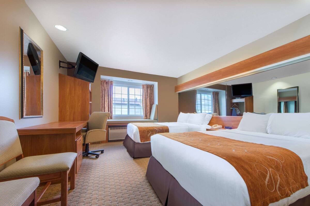 A hotel room with two beds, a desk, a chair, a TV, and a large mirror.