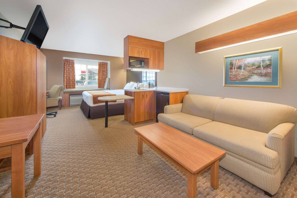 A compact living space with a sofa, a dining table, a kitchen area with a microwave, and a television.