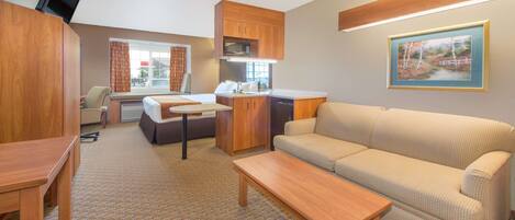 A compact living space with a sofa, a dining table, a kitchen area with a microwave, and a television.