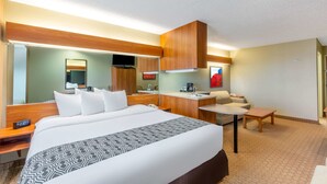 Une chambre d’hôtel avec un grand lit, un bureau, une chaise, une petite table, un canapé, une télévision et un miroir.