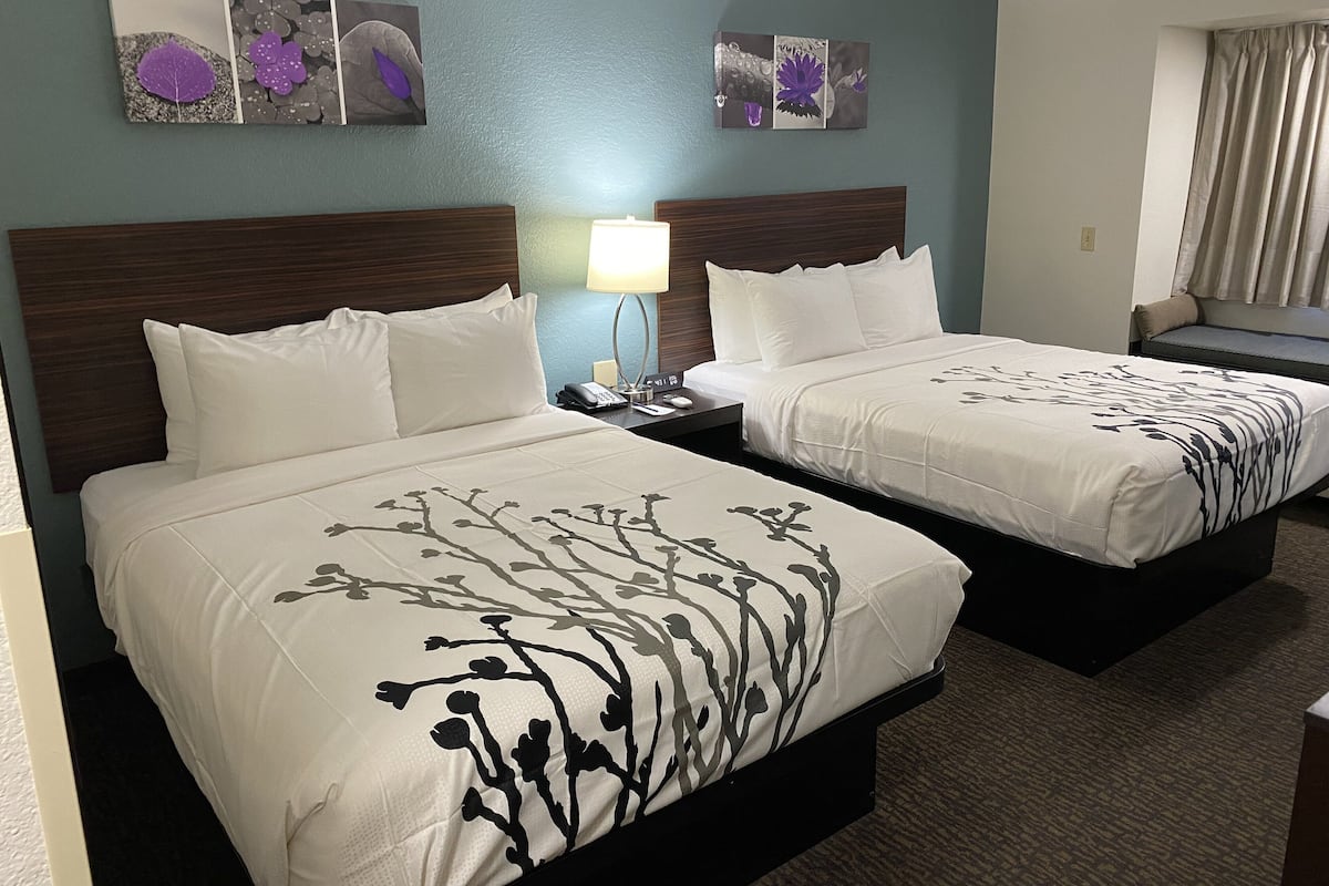 A hotel room with two beds, a nightstand with a lamp, and artwork on the wall.