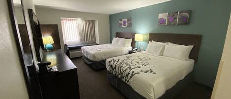 A hotel room with two beds, a desk, a lamp, and a window with curtains.