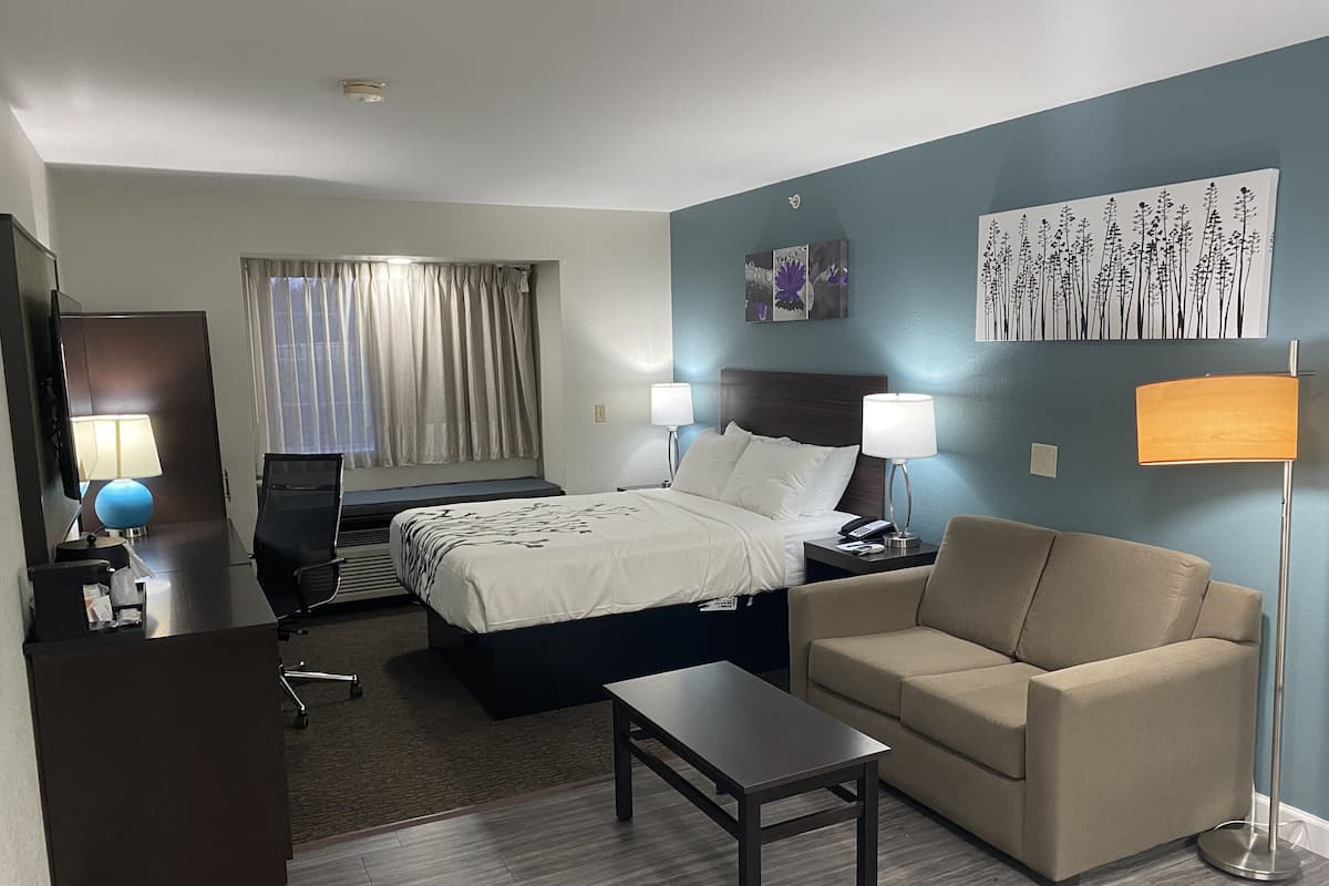 A hotel room with a bed, bedside tables, a desk, a chair, a lamp, a TV, and a window with curtains.