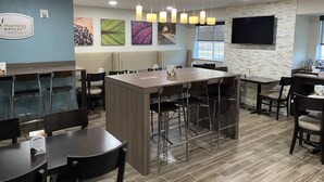 A modern breakfast area with a long communal table, individual seating, and a mounted TV. - Sleep Inn St. Robert-Fort Leonard Wood (St. Robert)