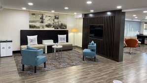 A modern hotel lobby with a sofa, chairs, a TV, and a patterned rug. - Sleep Inn St. Robert-Fort Leonard Wood (St. Robert)
