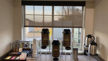 A coffee station with a window view, including coffee makers, milk dispensers, and coffee pods.